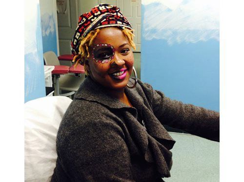 Smiling person in a colorful headwrap and glasses seated in a clinic room