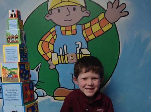 Child smiling in front of a colorful cartoon mural, with stacked blocks on the left.