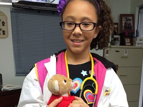 Girl in a white coat holding a teddy bear in a clinic or hospital setting