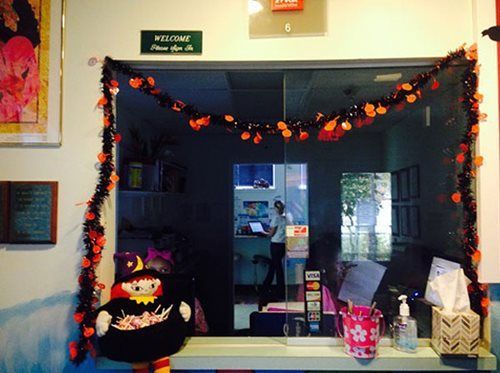 Halloween-decorated doorway with orange garland, pumpkins, and a person reflected in the dark glass interior