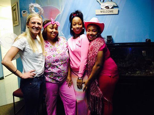Four women posing together indoors, dressed in colorful pink outfits and cowboy hats.