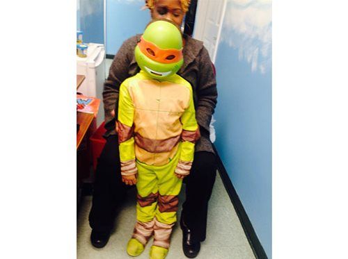 Child in a Teenage Mutant Ninja Turtles costume stands with an adult in a hallway.