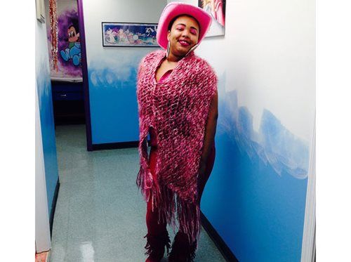 Person in a pink outfit and hat posing in a hallway with blue-and-white walls.
