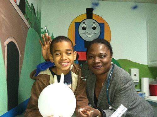 Smiling child and adult posing indoors beside a Thomas the Tank Engine mural and a white balloon