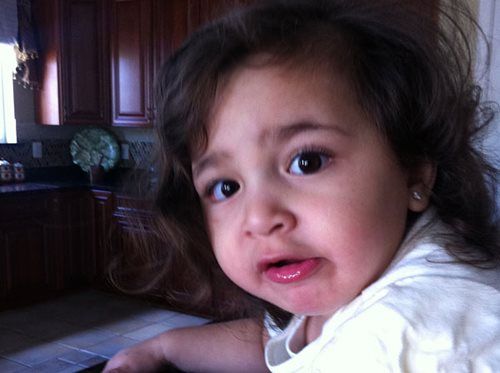 Close-up of a child with a surprised expression, leaning on a table in a dimly lit kitchen