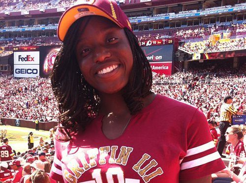 Smiling fan in a maroon baseball cap and shirt at a crowded basketball arena during a game