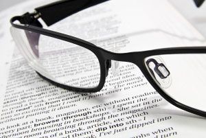 Black eyeglasses resting on an open book or document with printed text on the page.
