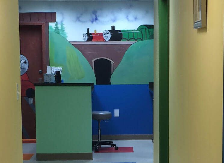 Colorful hallway with a mural of a red train above a tunnel, green walls, and a stool in front.