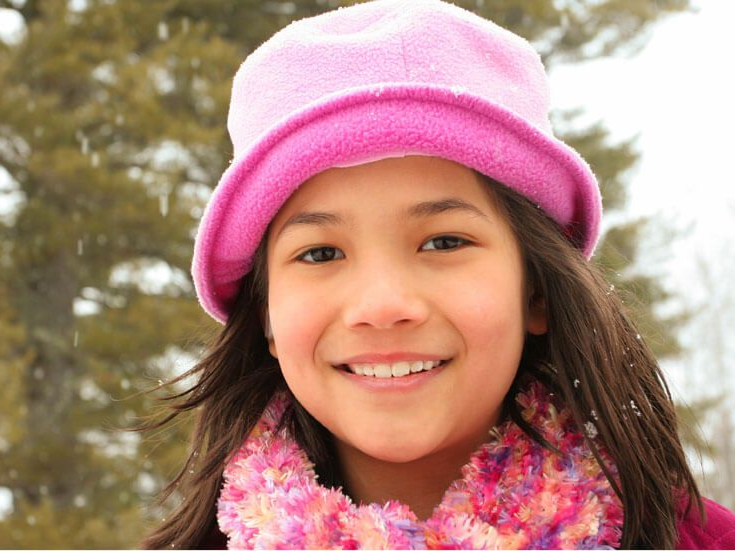 Smiling child in a pink hat and scarf outdoors in winter