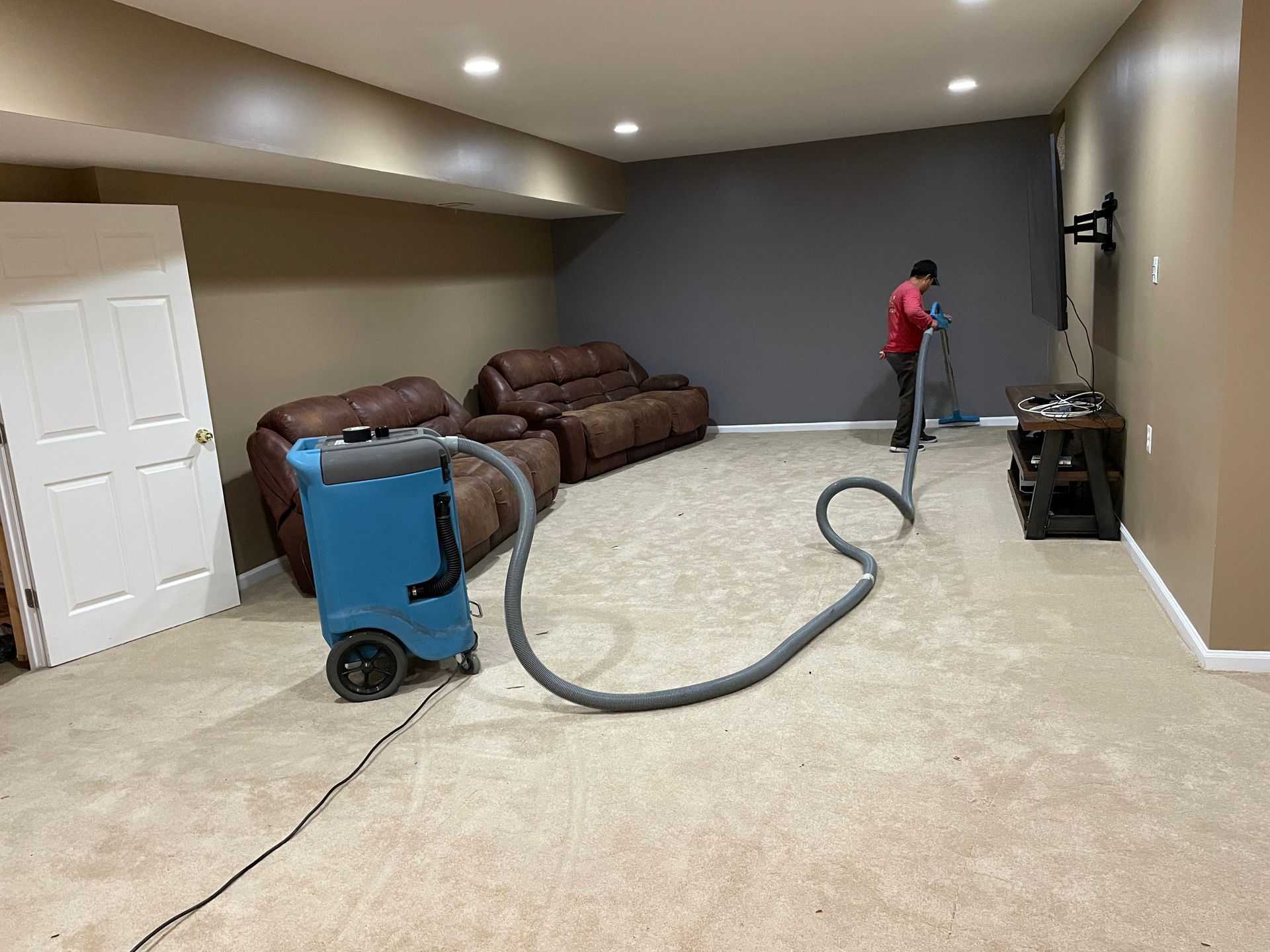 A man is cleaning a basement carpet with a vacuum cleaner.