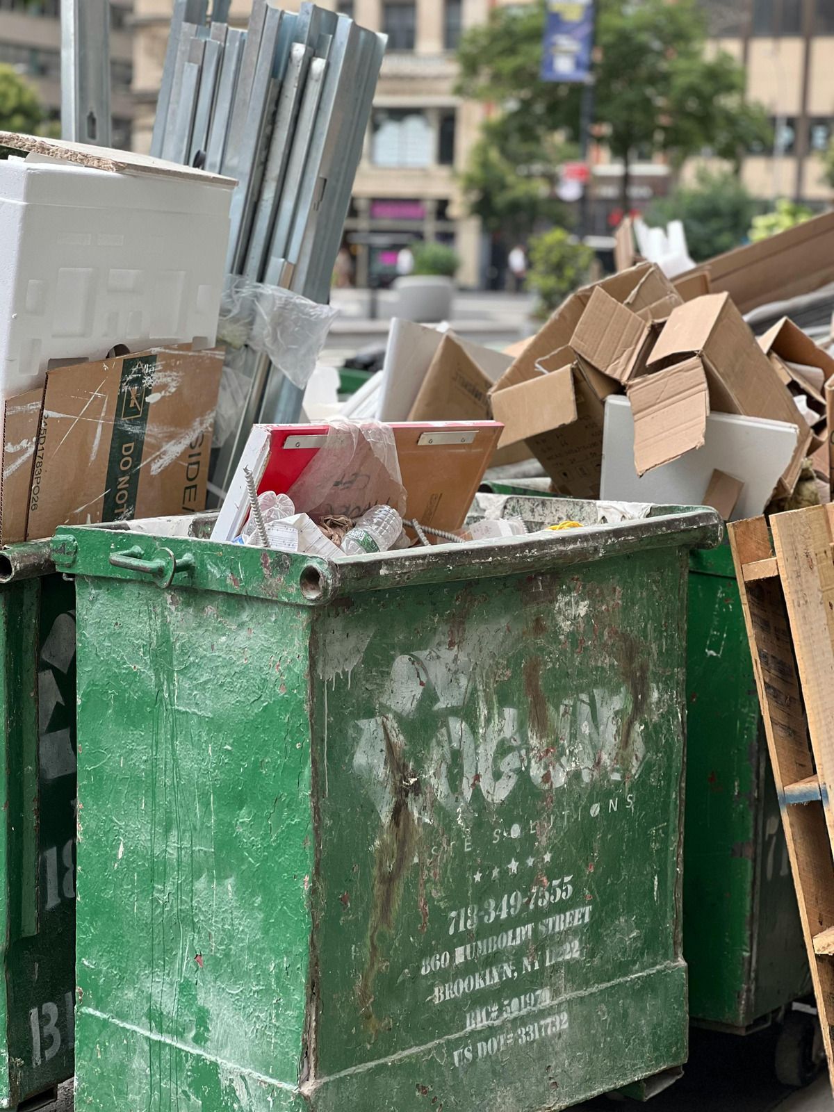 Green dumpster overflowing with cardboard boxes on a city street.
