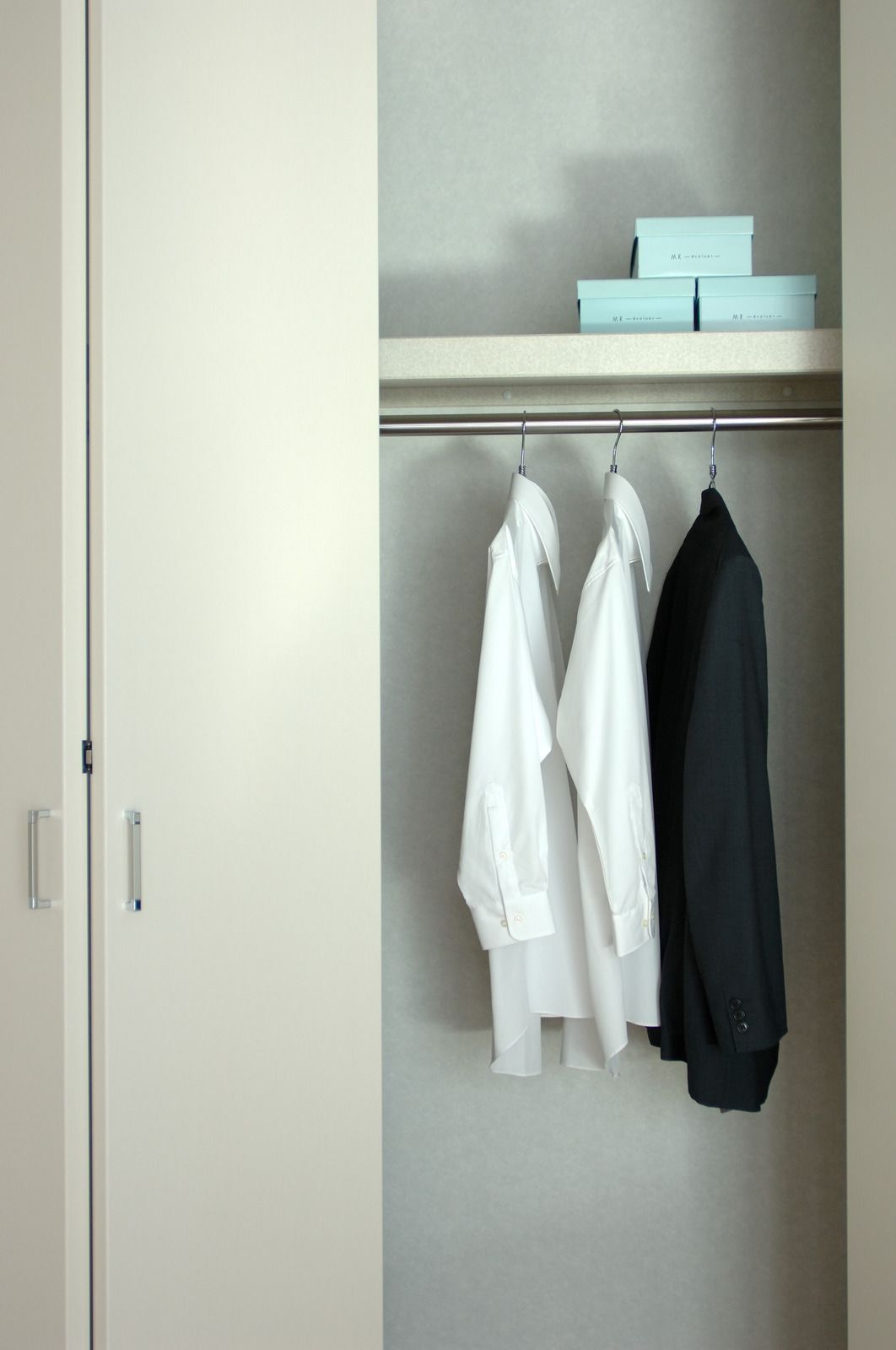 Closet with hanging white and black clothes and stacked light blue boxes on the shelf