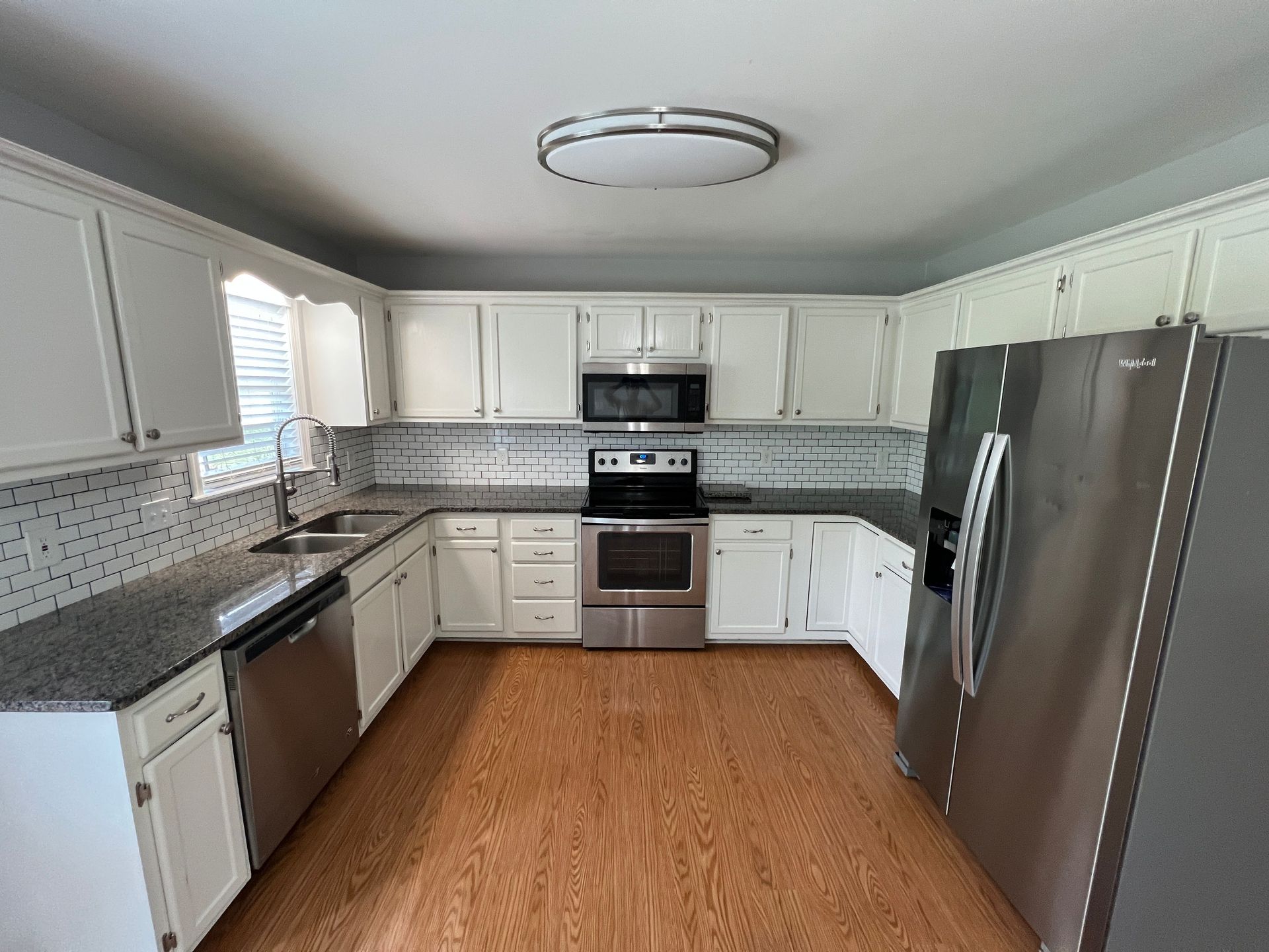 Modern white kitchen with stainless steel appliances, gray countertops, and wood flooring