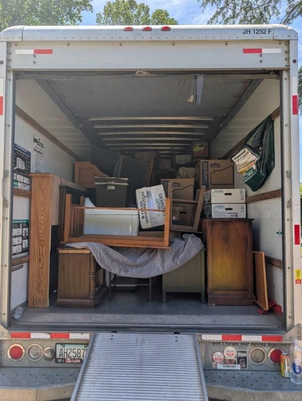 Open moving truck packed with furniture, boxes, and household items, ramp down at the back.