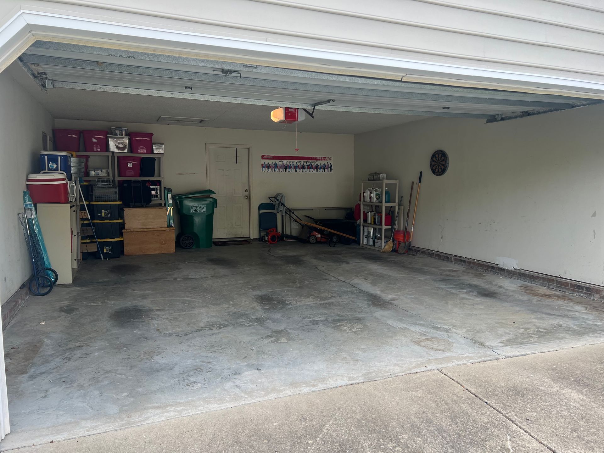 Empty garage with concrete floor, shelves of boxes and tools along the back wall, and an open door.