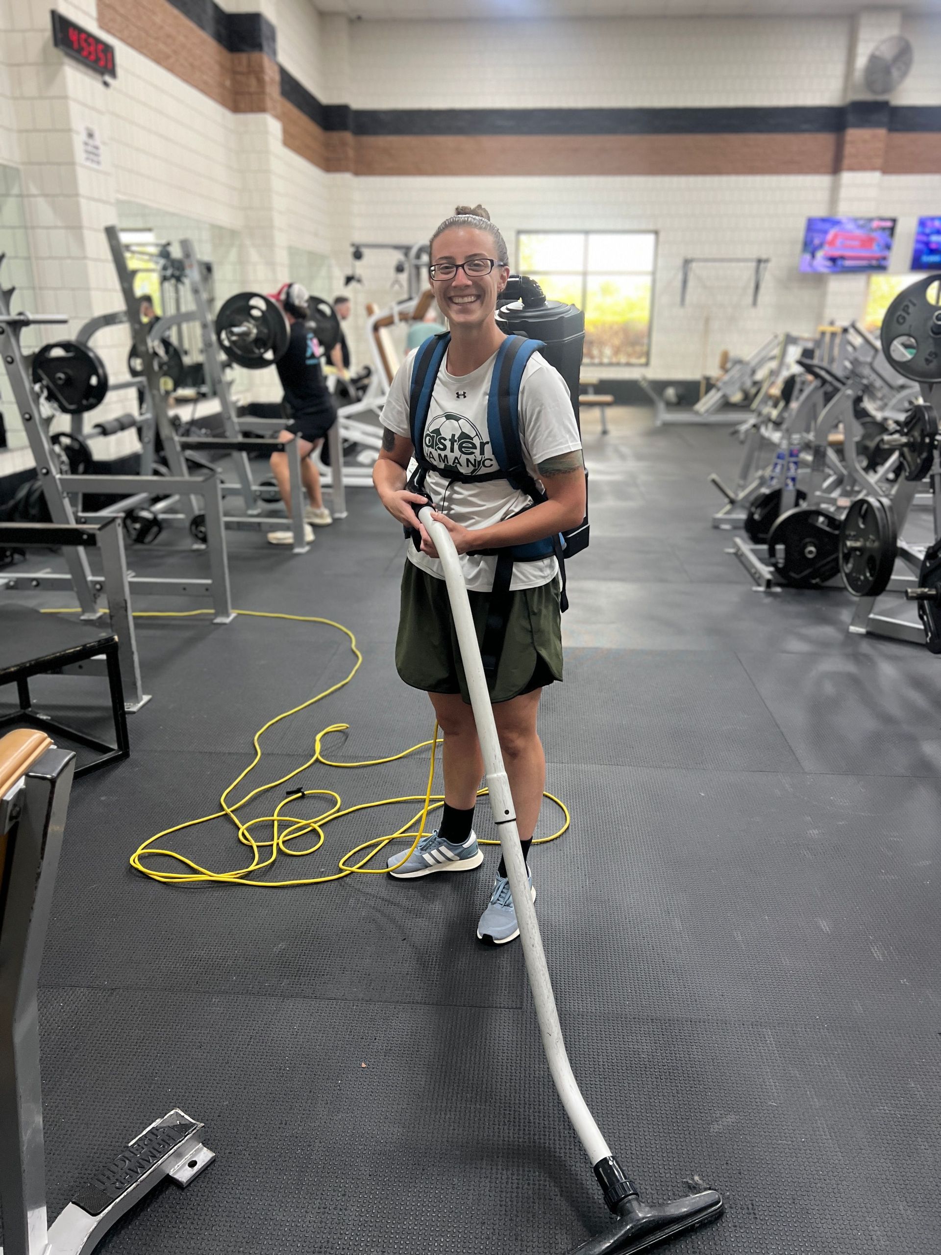Person using a floor-cleaning machine in a gym, with exercise equipment in the background.