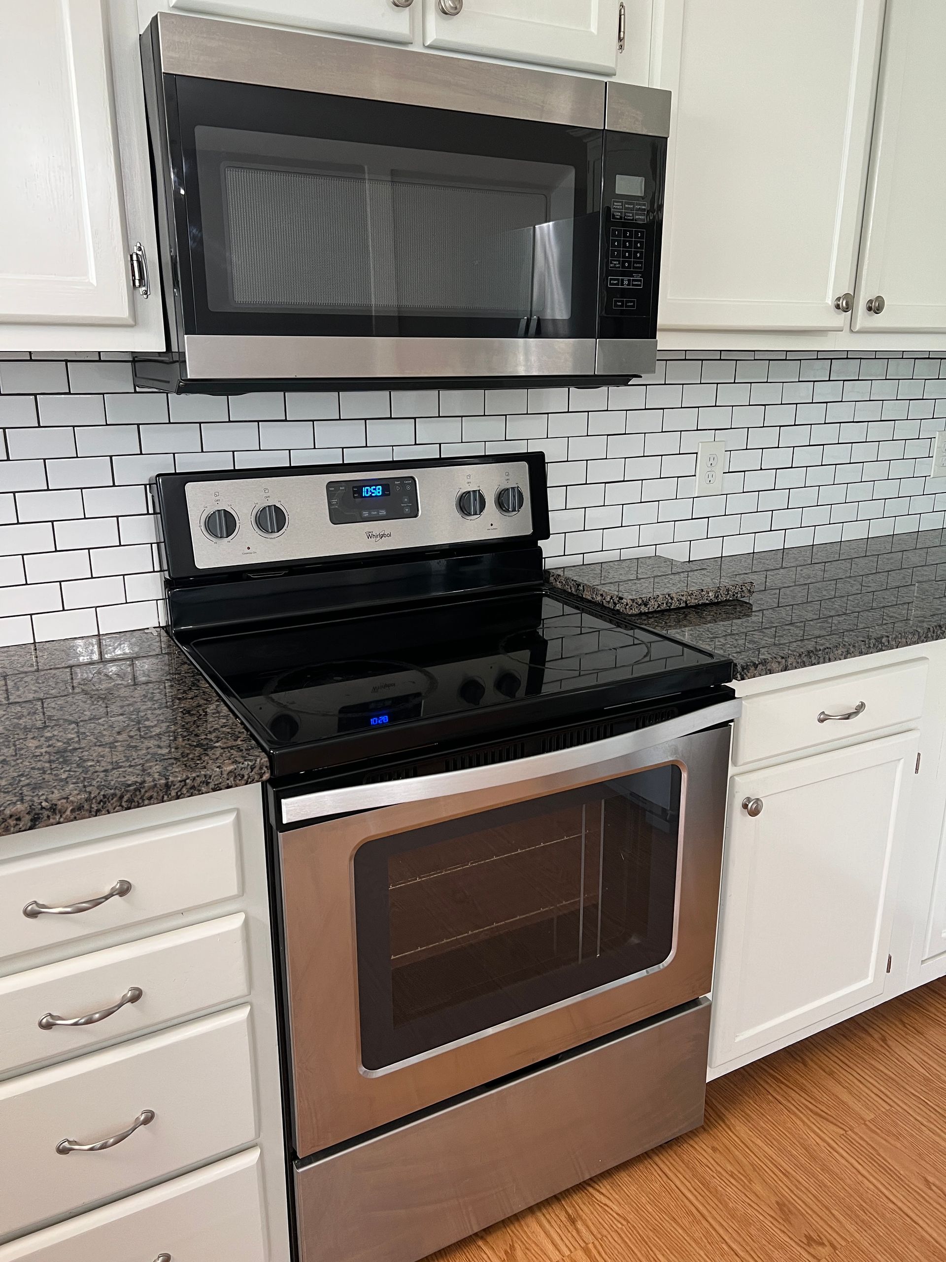 Modern kitchen with stainless steel stove, black microwave, white cabinets, and granite countertop