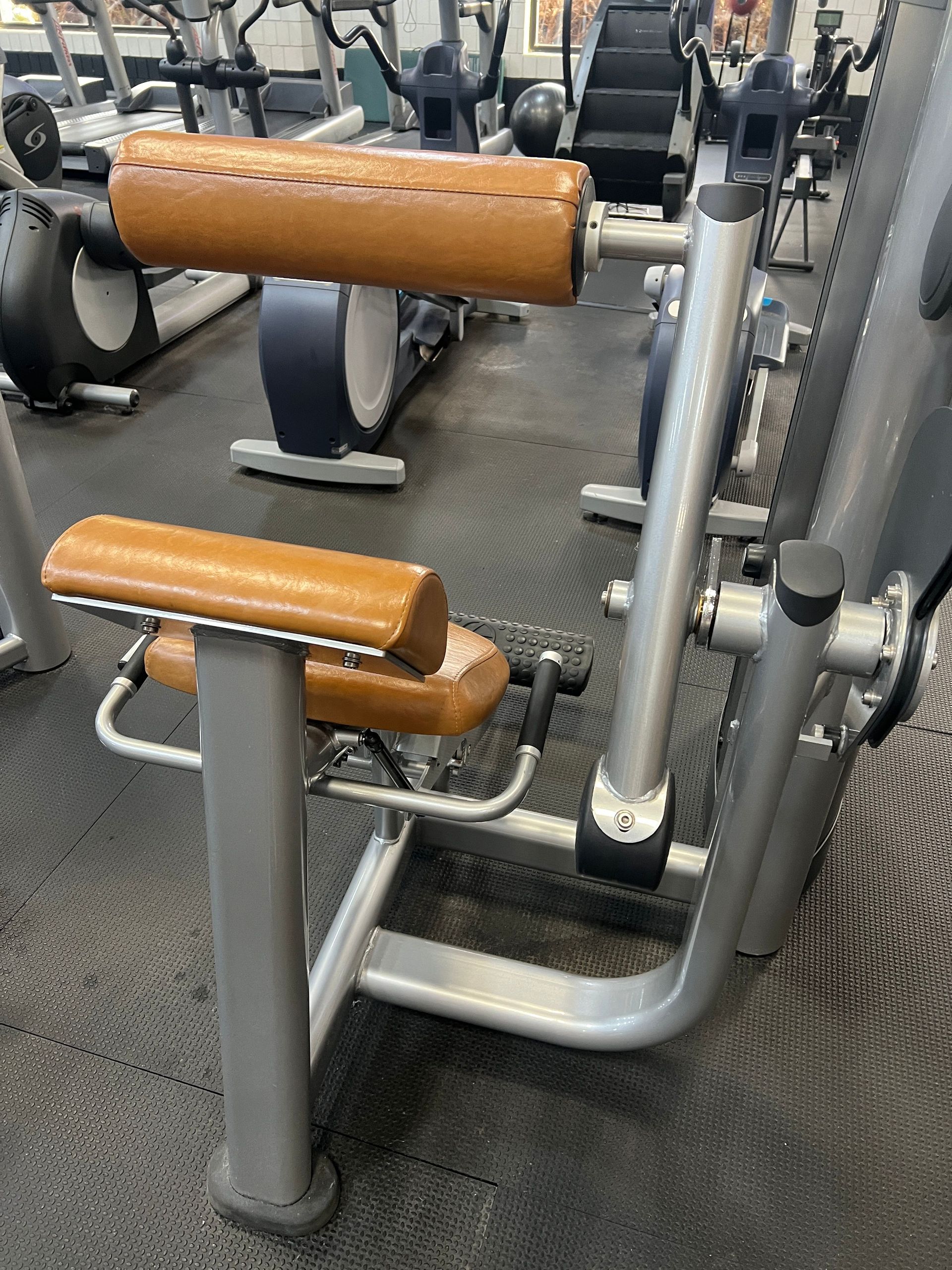 Gym workout machine with tan pads and silver frame on a black rubber floor