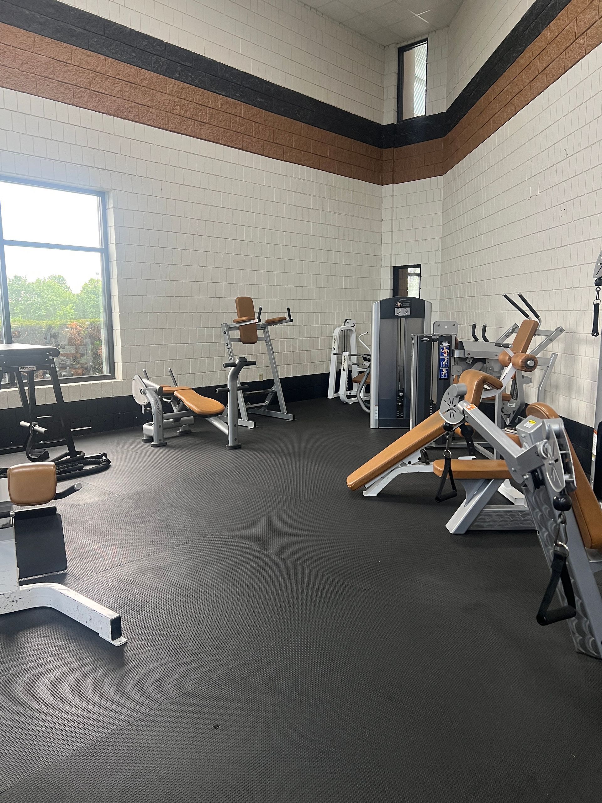 Modern gym with exercise machines, black flooring, and large windows letting in natural light