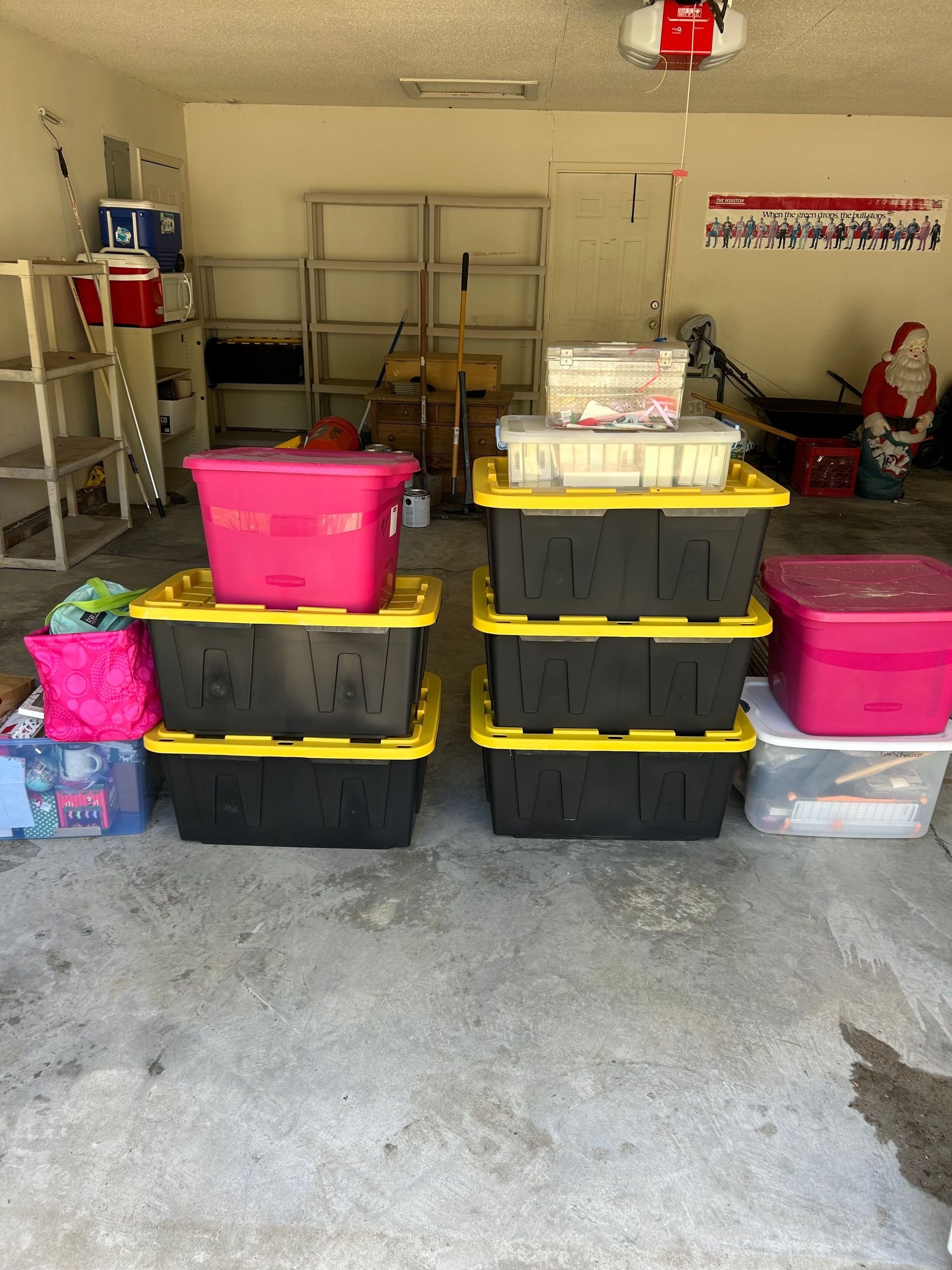 Garage filled with stacked plastic storage bins and tubs, with shelves and tools along the back wall.