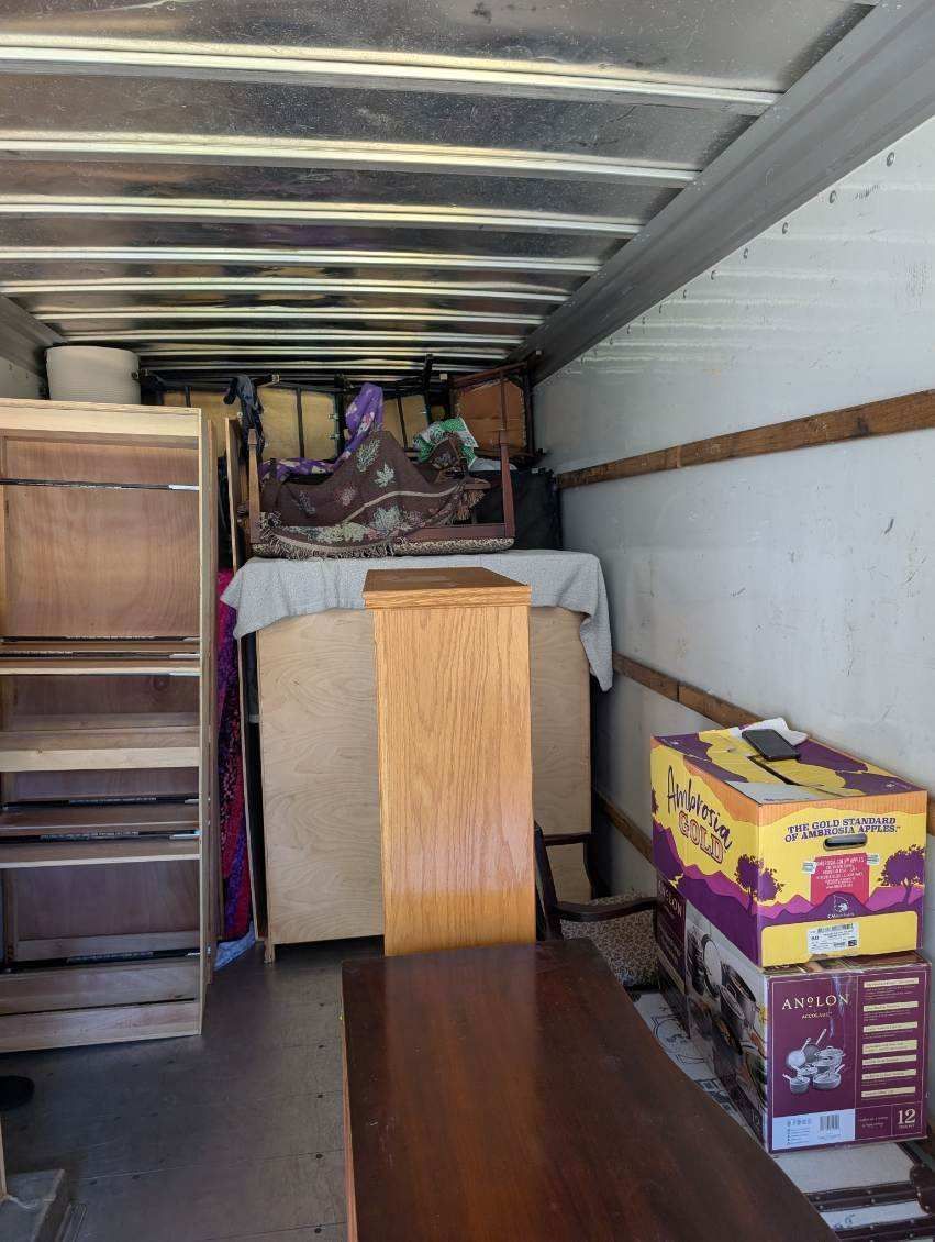 Loaded moving truck with stacked boxes, furniture, and a wooden cabinet in the back.