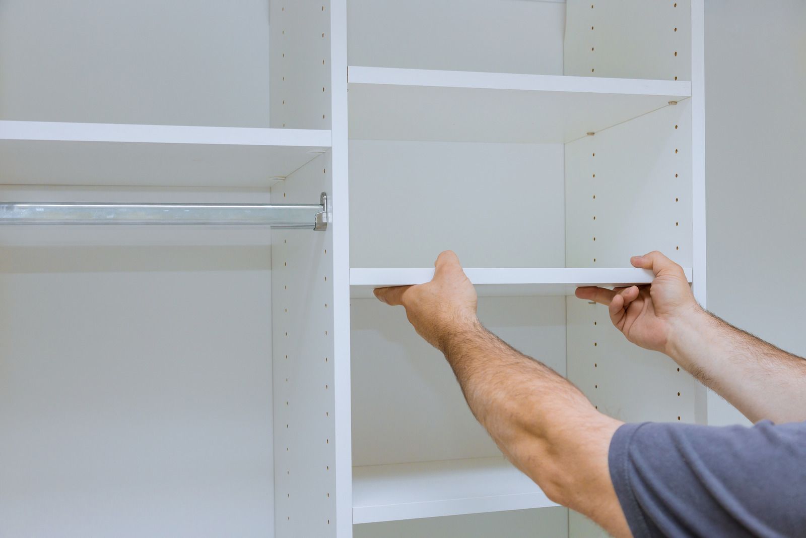 Hands installing a white shelf inside an empty closet.