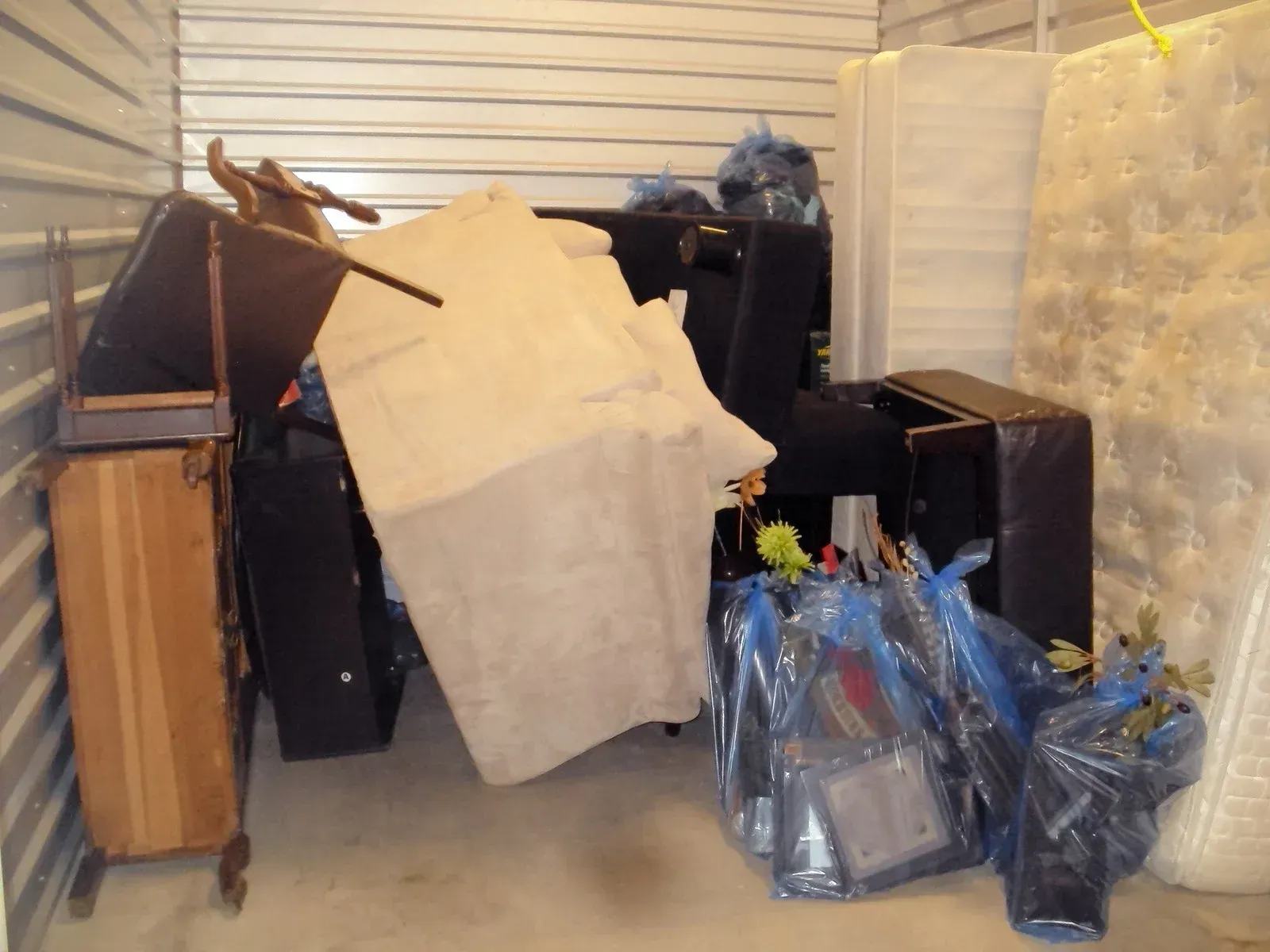 Cluttered storage area with furniture, boxes, and trash bags piled in front of a closed garage door