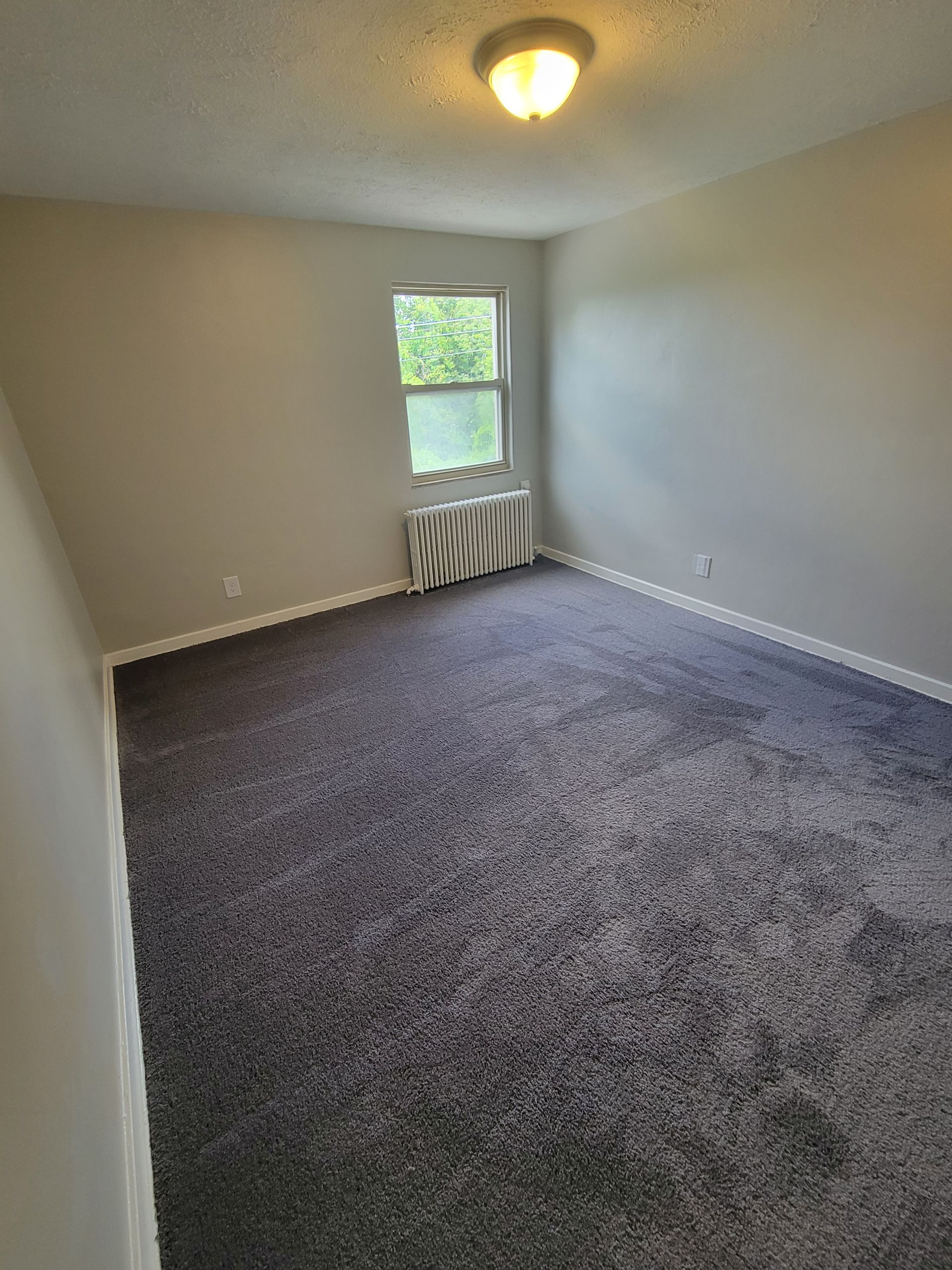 An empty bedroom with a gray carpet and a window.