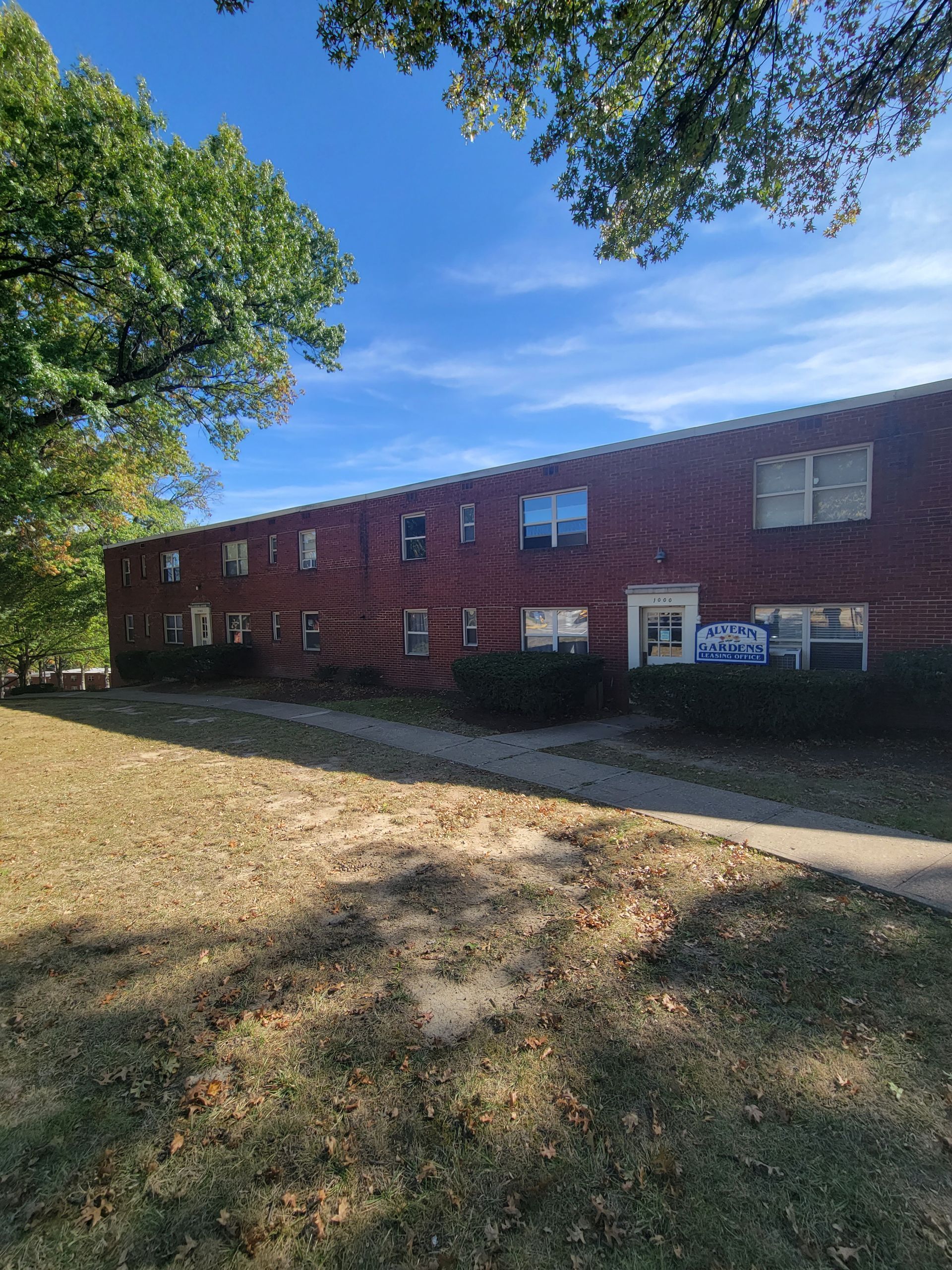 A large brick building with a lot of windows is surrounded by trees on a sunny day.