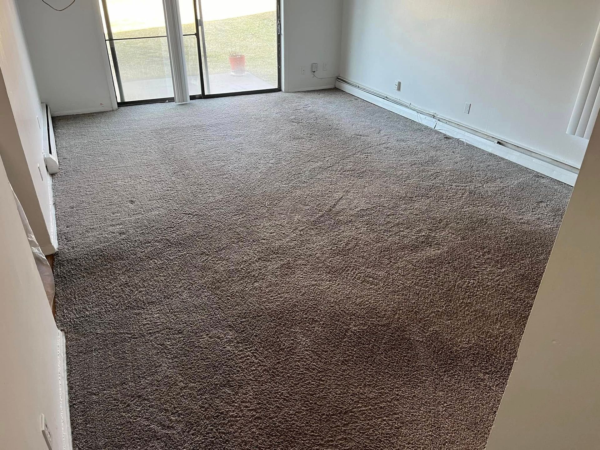 Empty carpeted room with white walls and sliding glass doors leading outside.