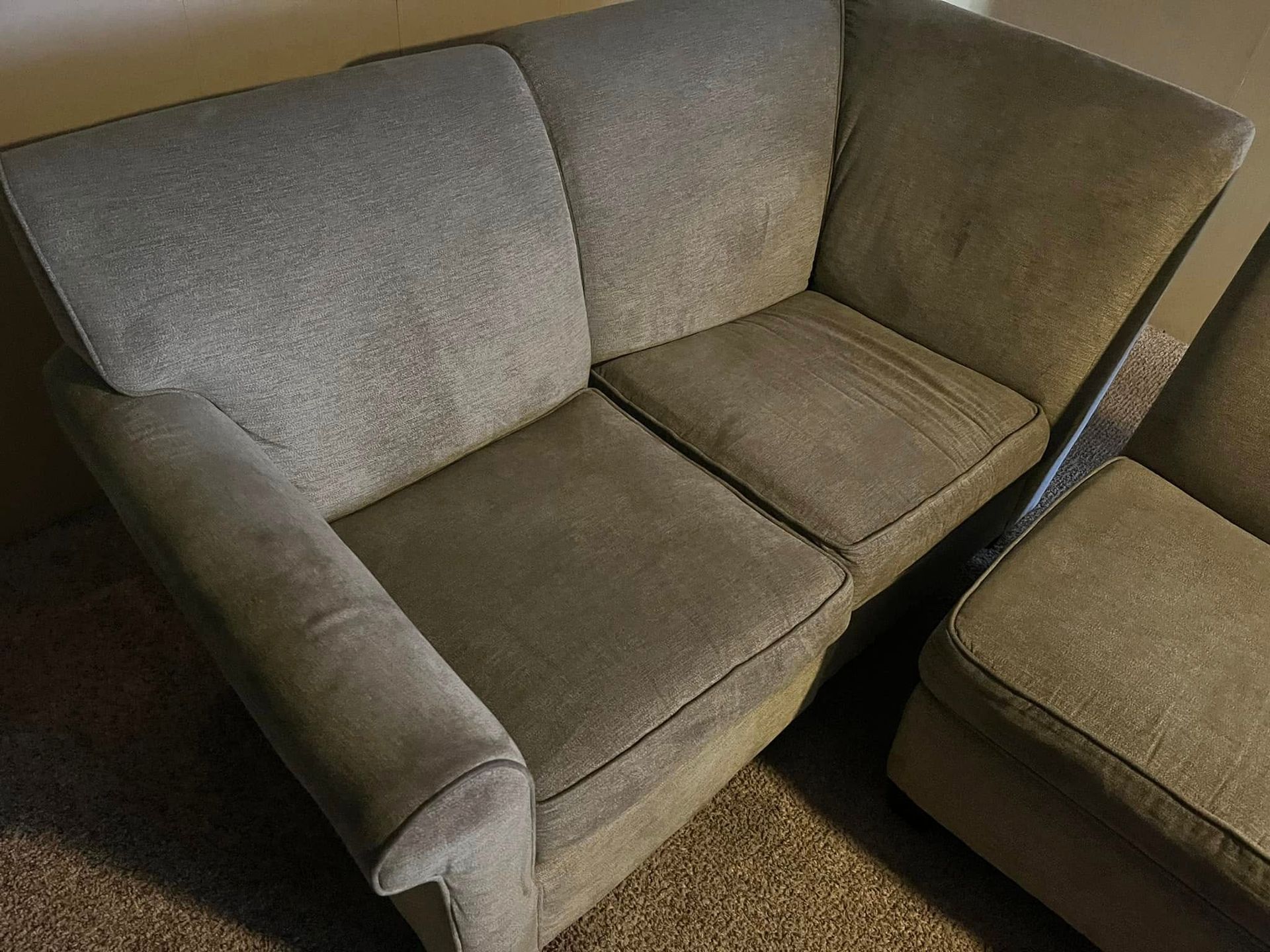 Top-down view of a beige two-seat couch with worn cushions and a dark chair edge beside it