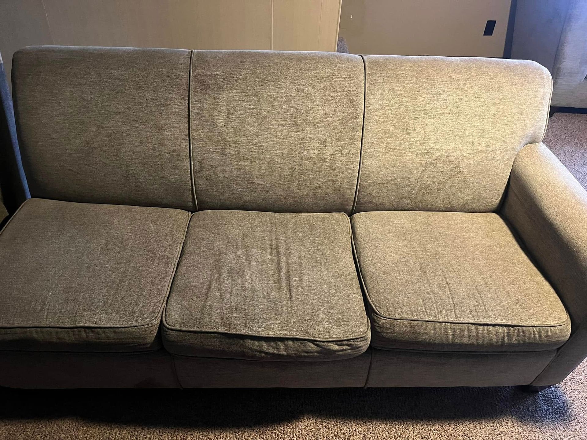 Beige upholstered sofa with dark base against a plain wall, photographed indoors.