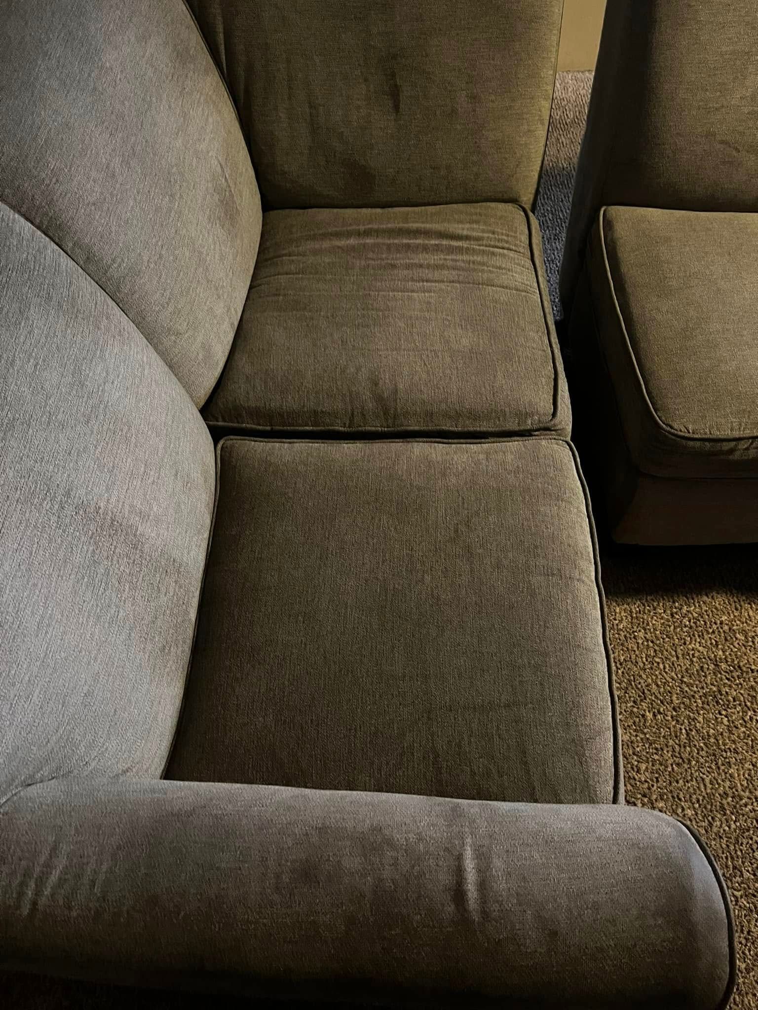 Close-up of a gray upholstered sofa with cushions and rounded armrest beside a brown chair
