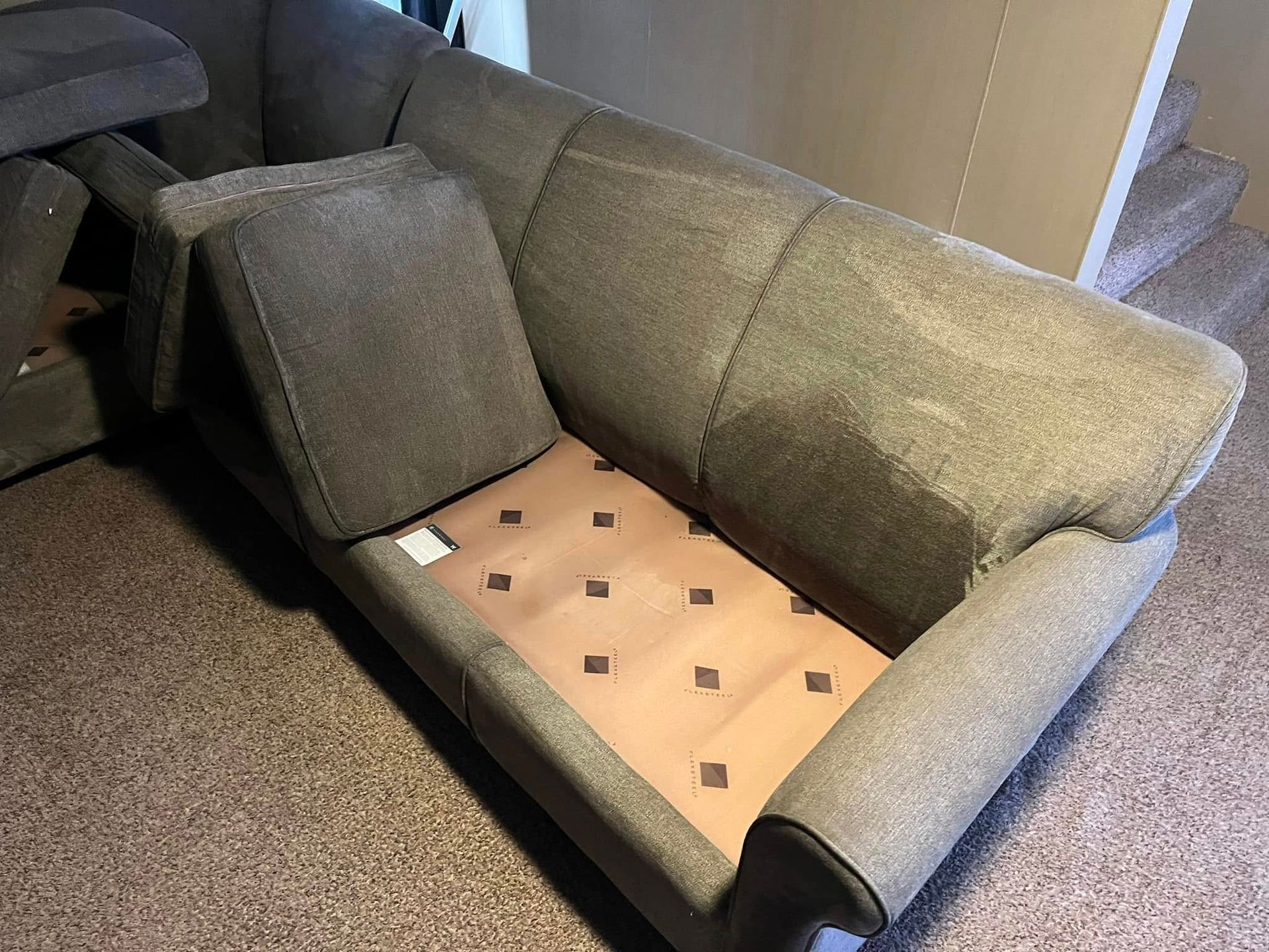 Gray sofa with a missing cushion, exposing a bare tan seat frame and one loose back pillow.
