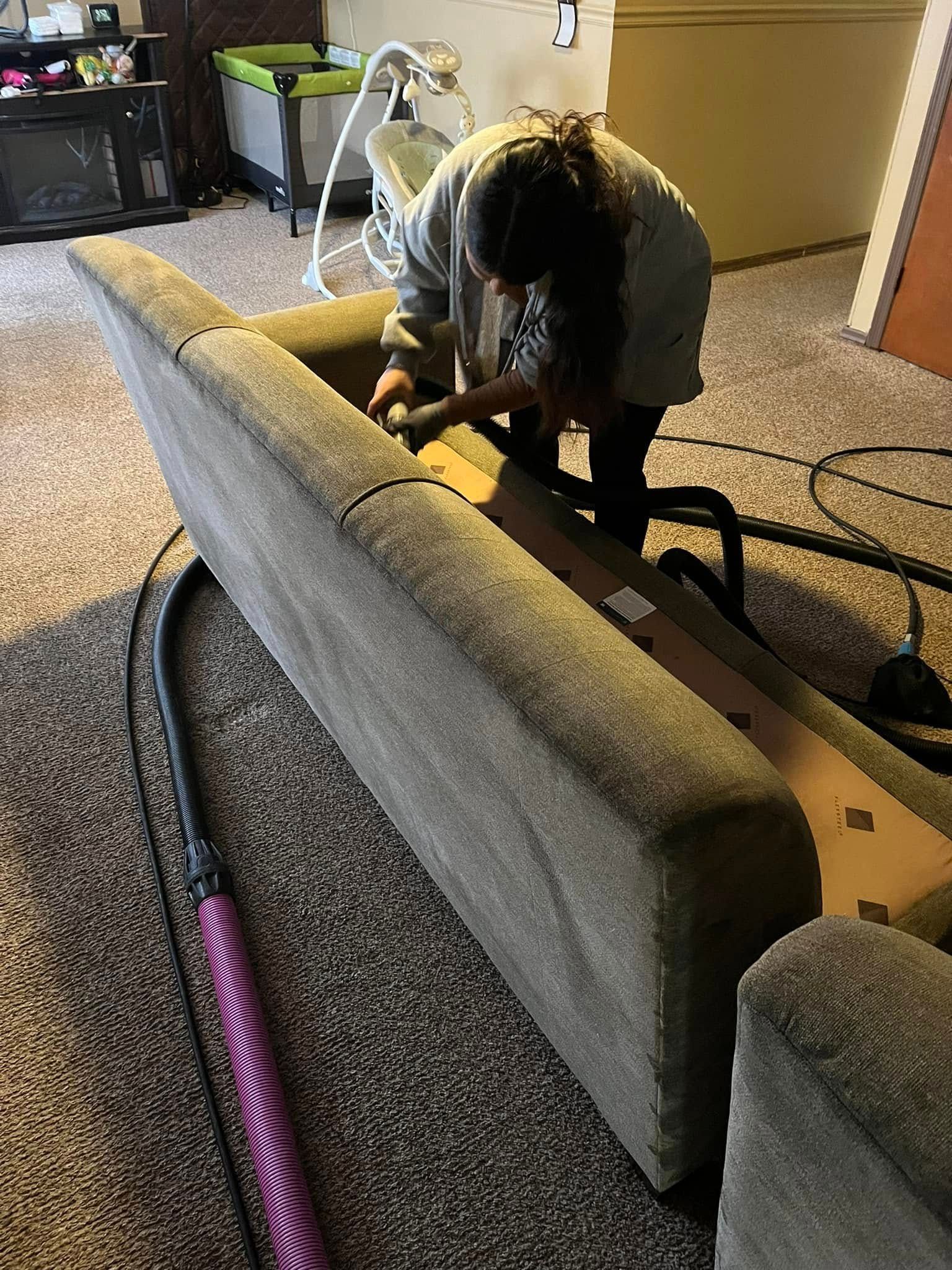 Person working on a gray couch frame in a carpeted room with tools and a vacuum nearby