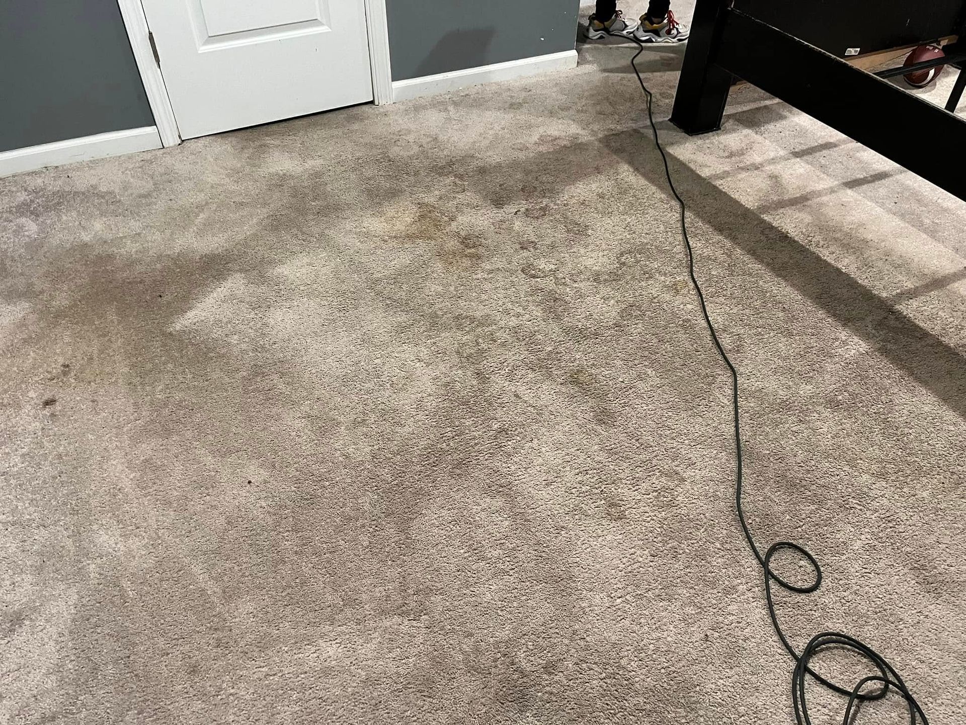 Carpeted bedroom floor with a loose black cable near a white door and bed frame.