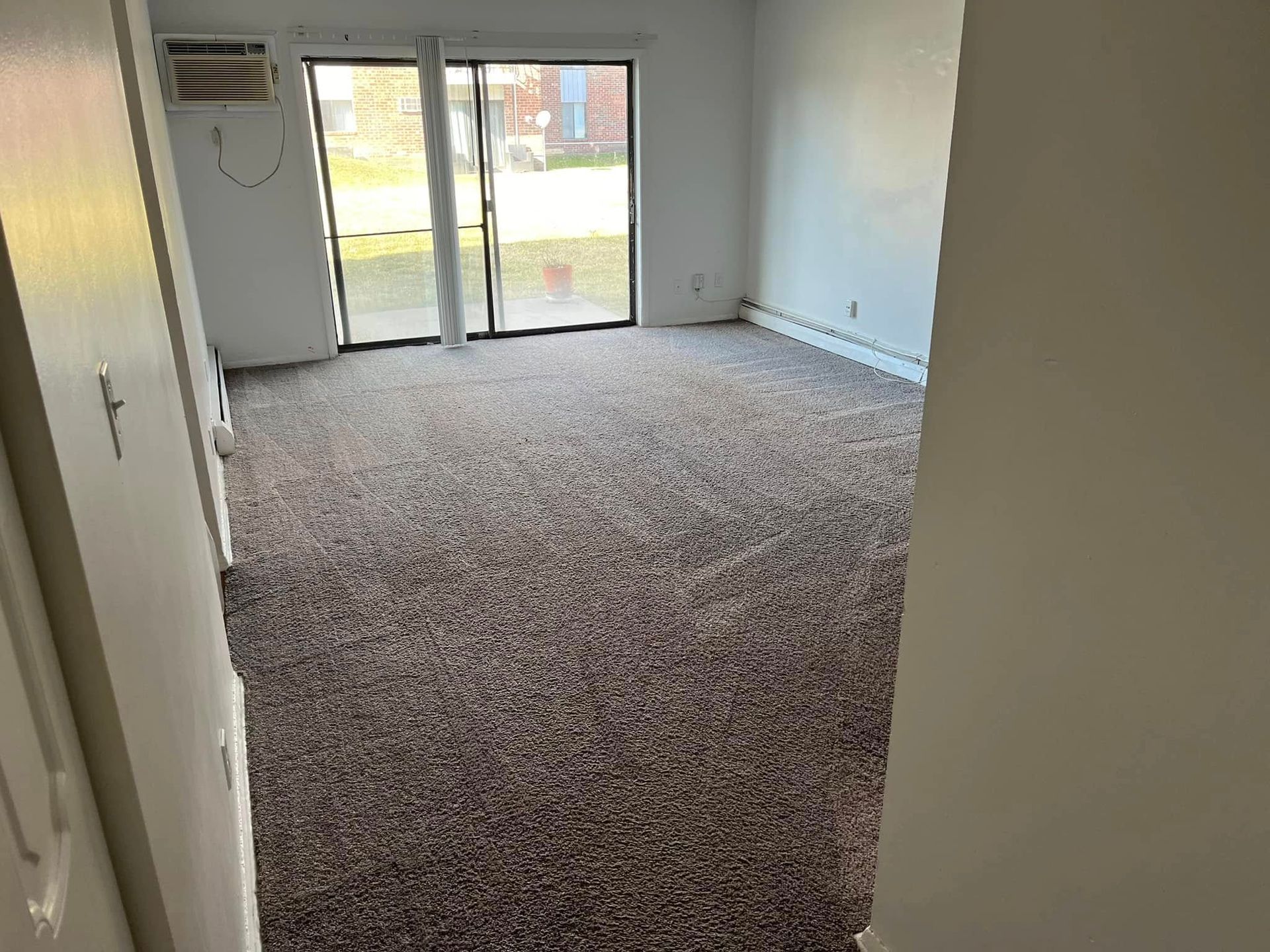 Empty carpeted living room with sliding glass doors and a front door opening to the outside