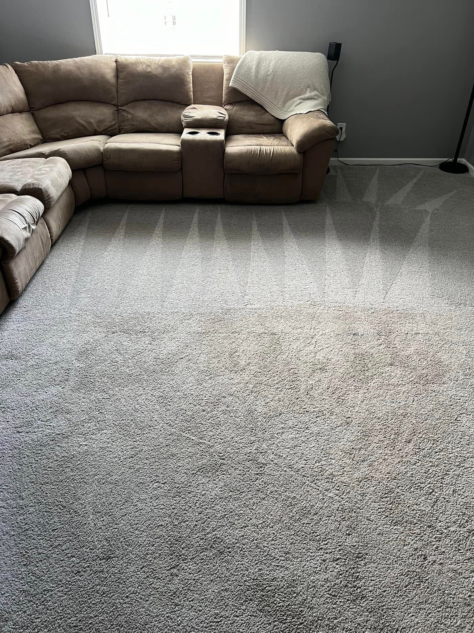 Living room with beige sectional sofa and a large gray carpet under bright window light