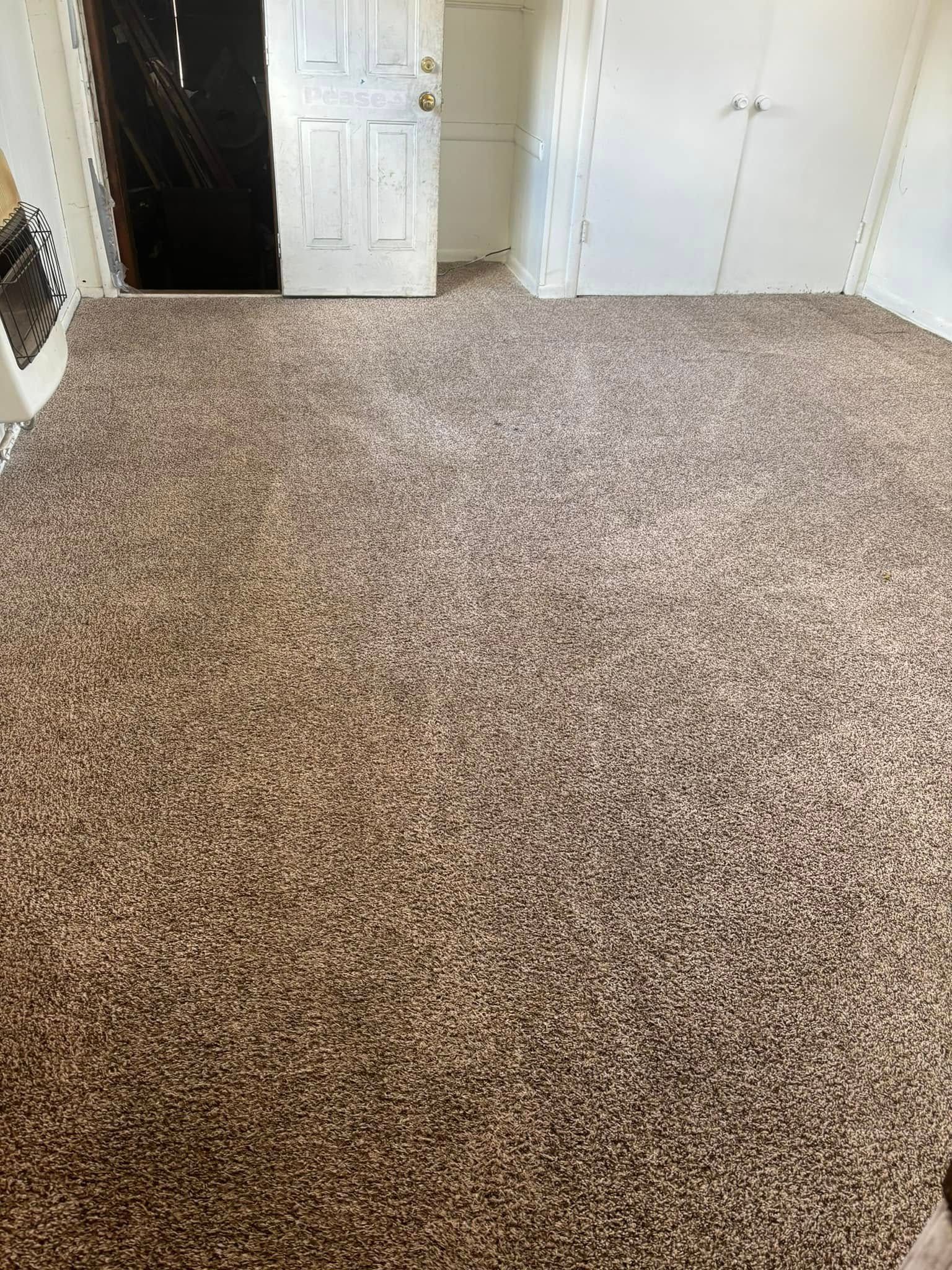 Empty carpeted room with white walls and an open doorway, lit by natural light.