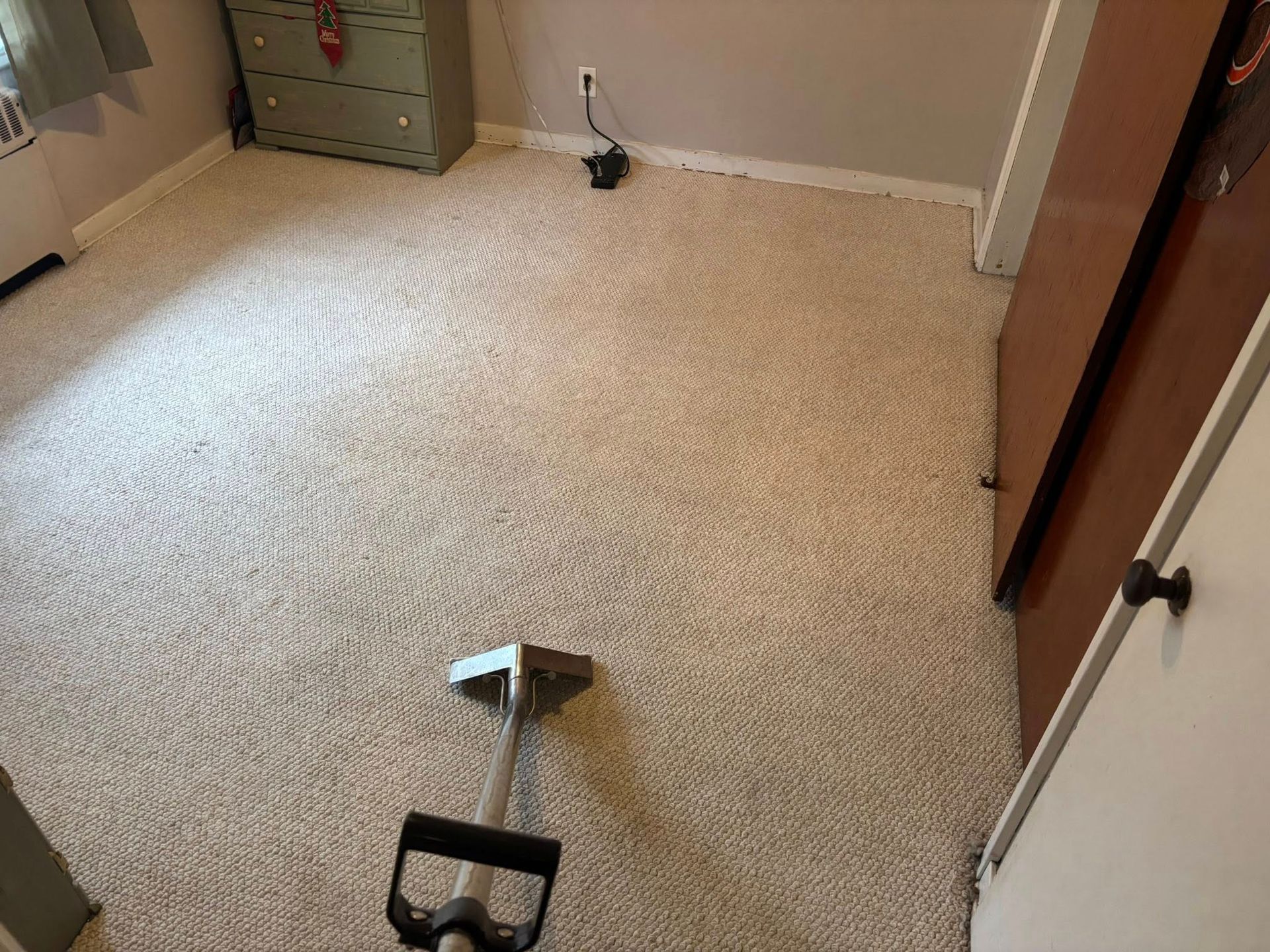 Carpeted room with a shovel and dustpan in the foreground and a small object against the far wall.