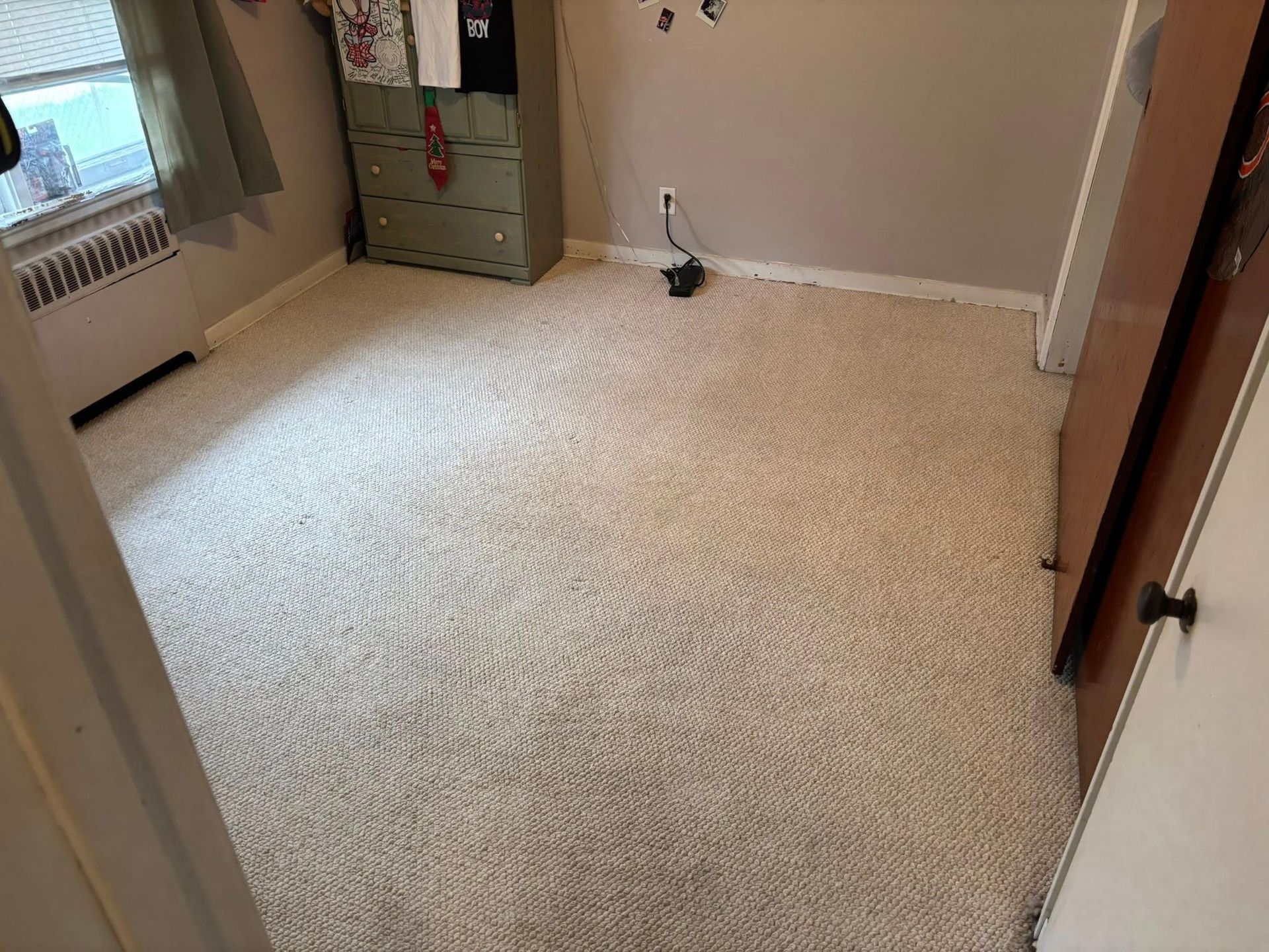 Empty beige-carpeted bedroom with green dresser, window, and open door