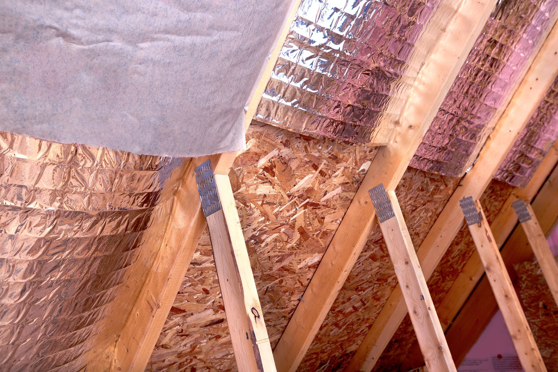 Wooden rafters and insulation in an attic space; silver reflective material visible.