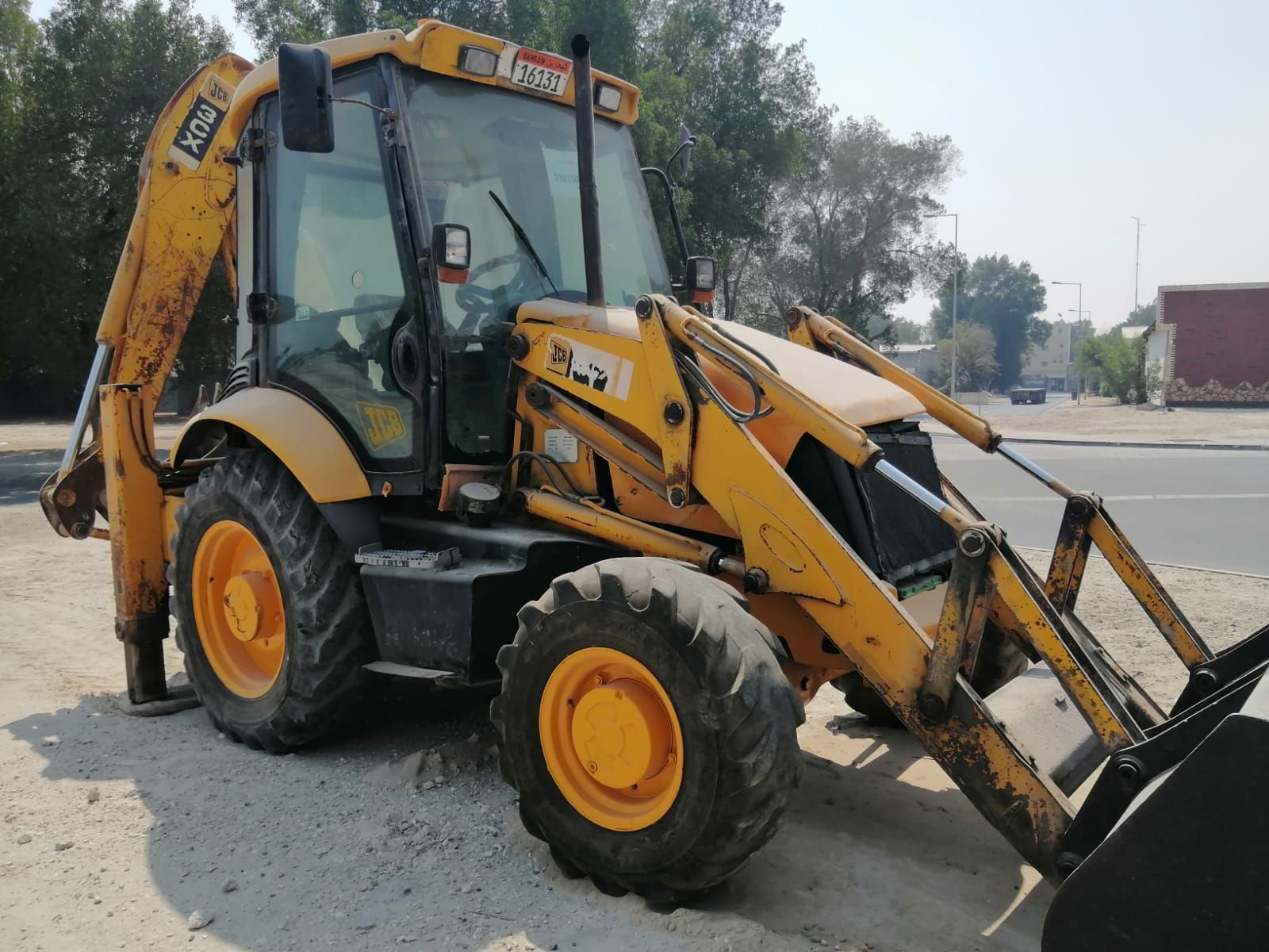 Yellow JCB backhoe loader parked on a paved road, outdoors, delirio heavy equipment