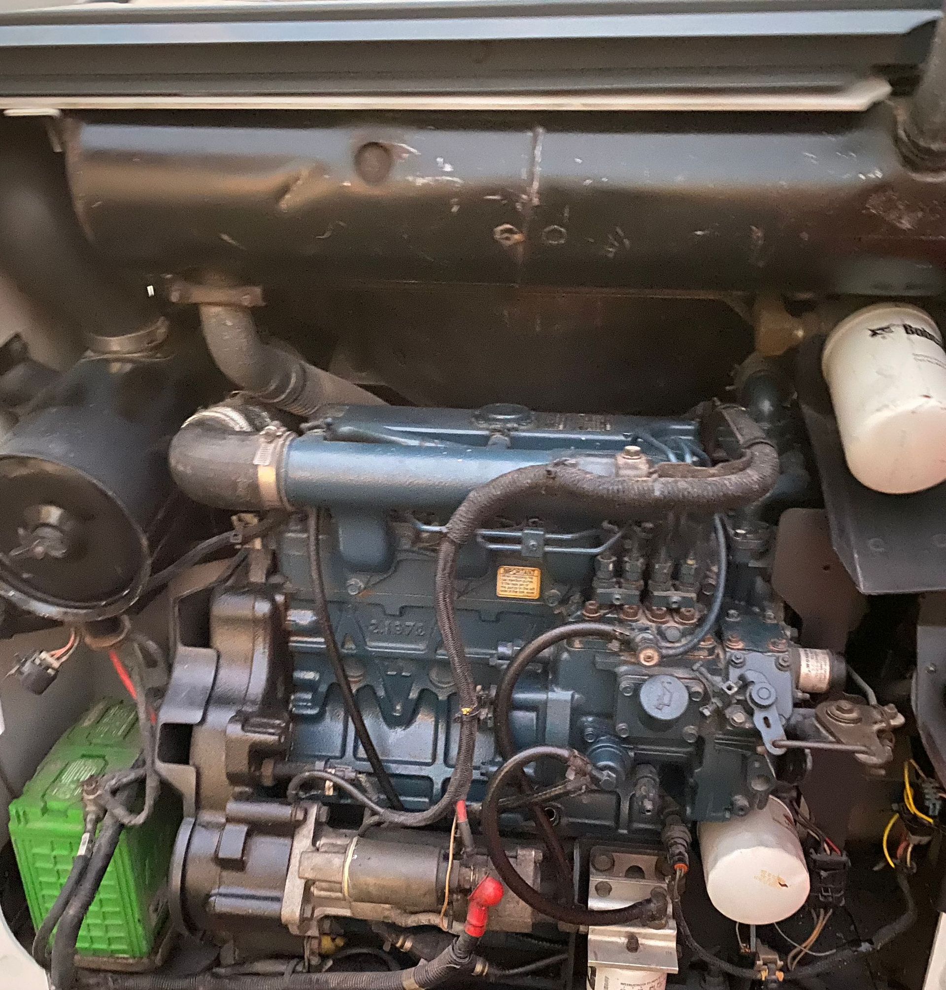 Close-up of a Kubota engine in a machine. Mostly dark blue and black components. Green battery on the left.