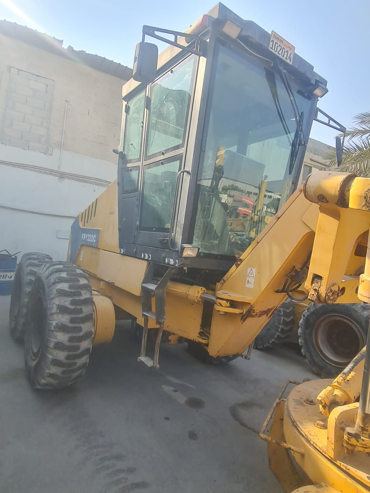 Yellow motor grader parked, with glass cab, and large tires.