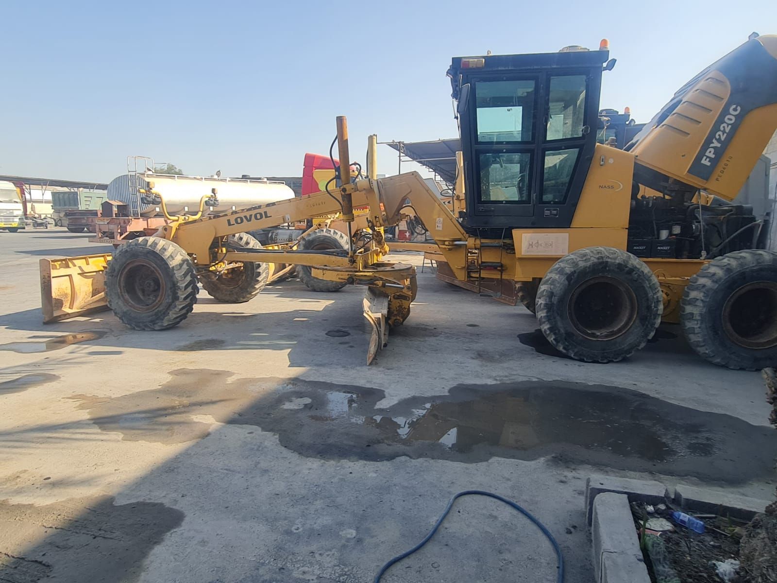 Yellow motor grader parked on a concrete surface, deliriomachinary