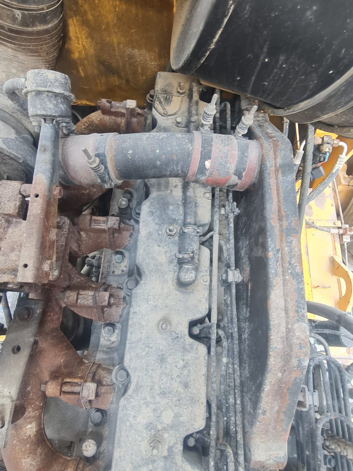 Close-up of a dusty industrial engine with black pipes, clamps, and various components.