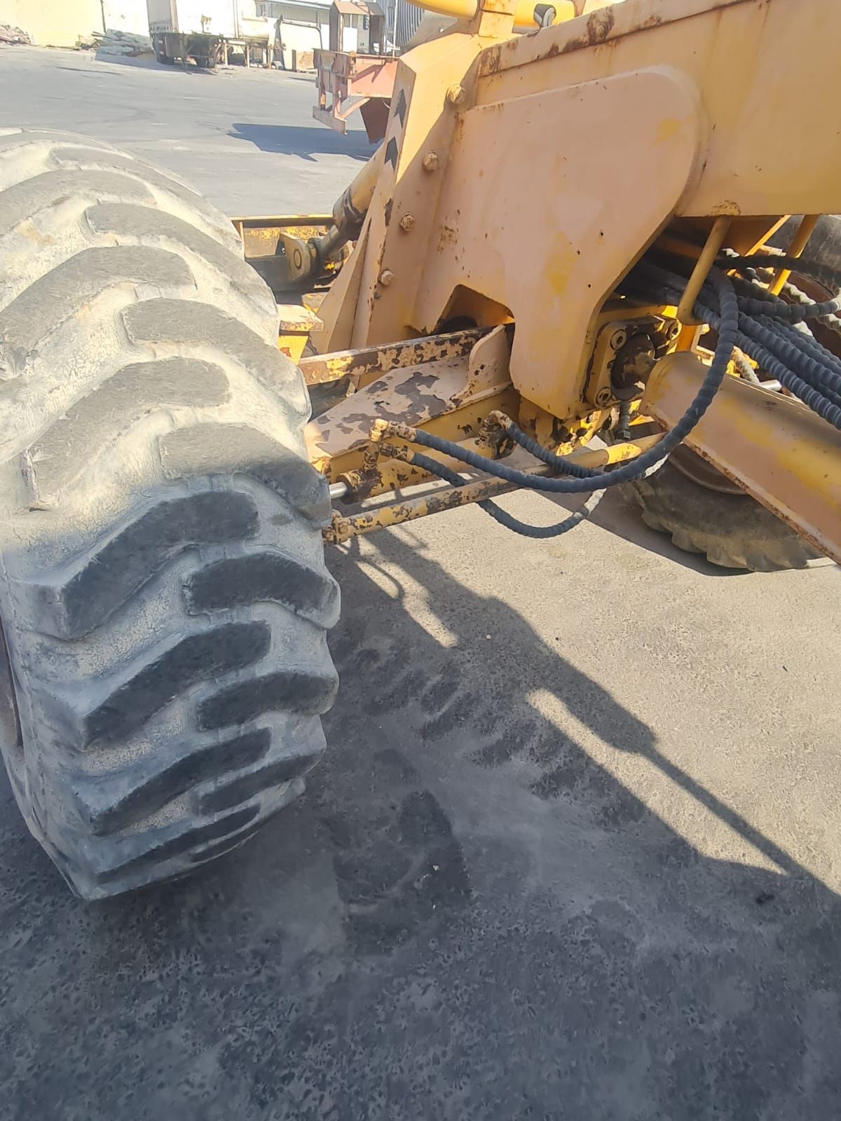 Yellow construction grader tire and machinery on asphalt.