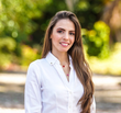 Mujer sonriente con una blusa blanca de pie al aire libre, con un fondo verde desenfocado