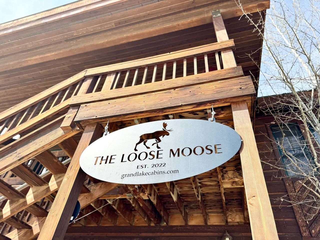Two-story brown wood building with exterior staircases, surrounded by trees and a dirt parking area.